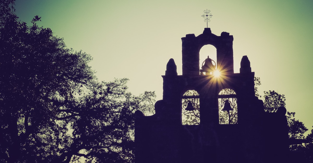 The sun rising and peeking through the window of the silhouette of a Spanish bell tower in San Antonio.